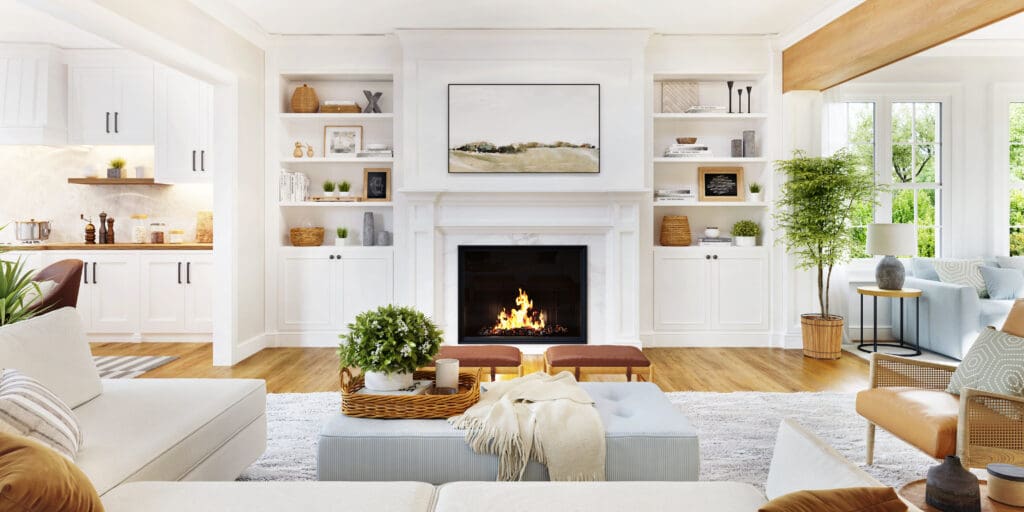 A bright, modern living room with a burning fireplace surrounded by white built-in shelves. The space includes a beige sofa, a large rug, and natural light streaming through large windows. Decor includes plants, books, and artwork.