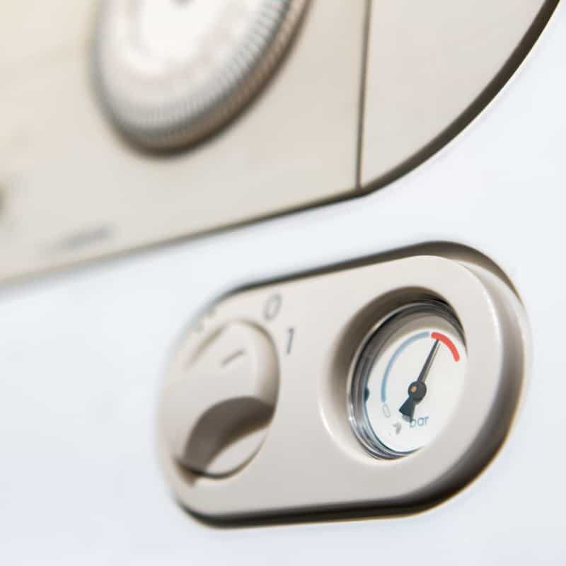 Close-up of a boiler control panel showing a round pressure gauge with the needle in the optimal range and a nearby rotary dial with settings marked 0 and 1.