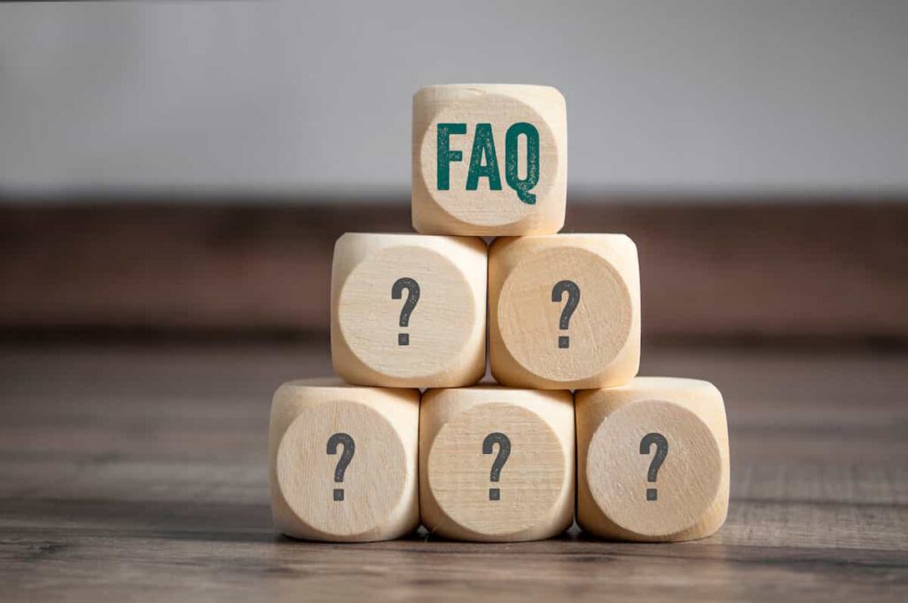 A pyramid of six wooden blocks, five with question marks and one on top labeled "FAQ," set against a blurred background.
