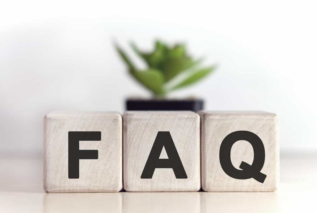 Three wooden blocks with the letters "F", "A", and "Q" are displayed side by side on a table, with a small green potted plant blurred in the background.